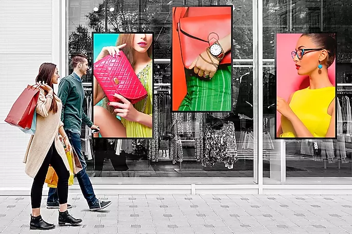 Digital screen displaying fashion ads in a retail window.